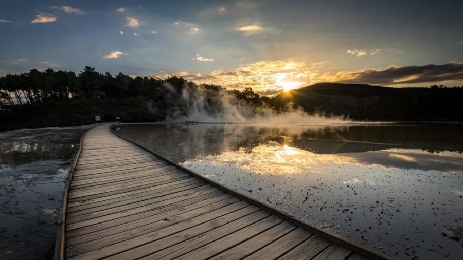 Steaming geothermal boardwalk at Wai-O-Tapu with sunset reflecting on hot spring pools in Rotorua, New Zealand