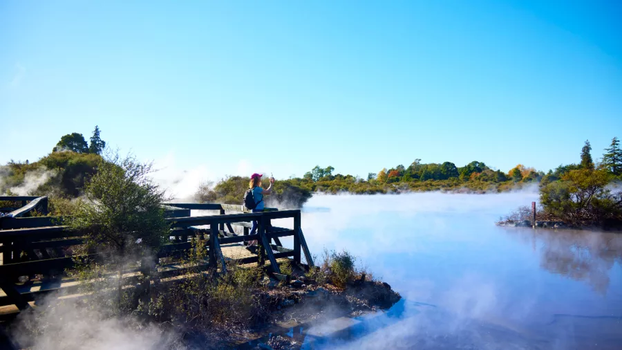 Visitor standing on viewing deck overlooking geothermal lake at Whakarewarewa Māori Village, Rotorua