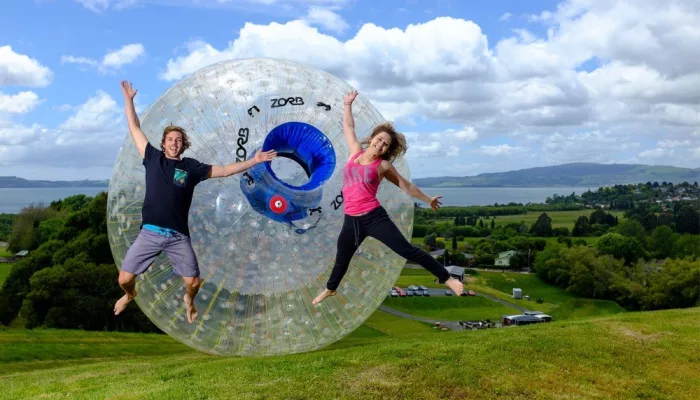 Two riders jumping in front of ZORB ball on the Mega Track with lake views in Rotorua