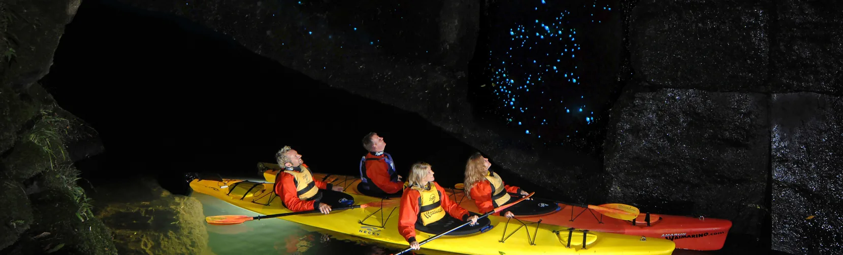 Group kayaking at night through a glowworm-lit cave near Tauranga, Bay of Plenty, New Zealand