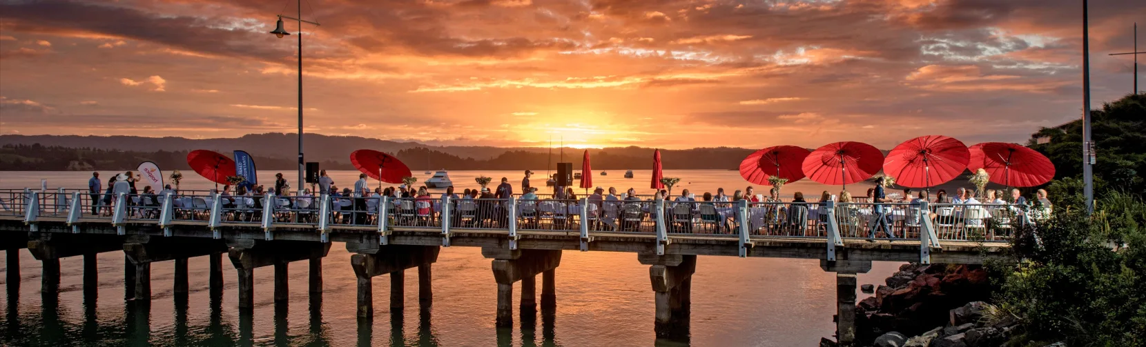 People gathered on Ohope Wharf at sunset in the Bay of Plenty, New Zealand
