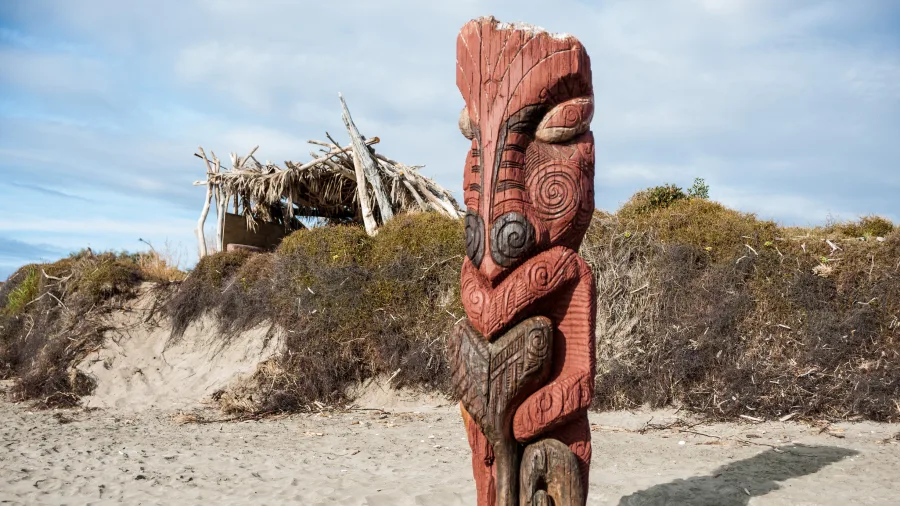 Intricately carved Maori pouwhenua standing on a Bay of Plenty beach in New Zealand
