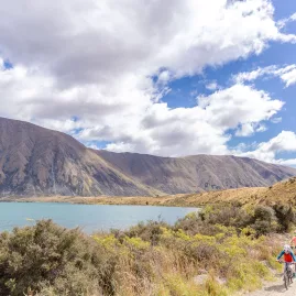 A group of cyclists, including children, riding next to the shoreline of Lake Ohau.