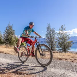 Cyclist performing a wheelie on a gravel trail above Lake Pukaki.