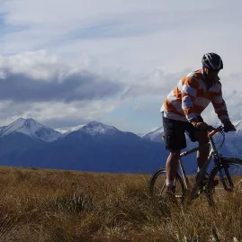 Mountain biker rides through golden tussock in high country terrain near Omarama.