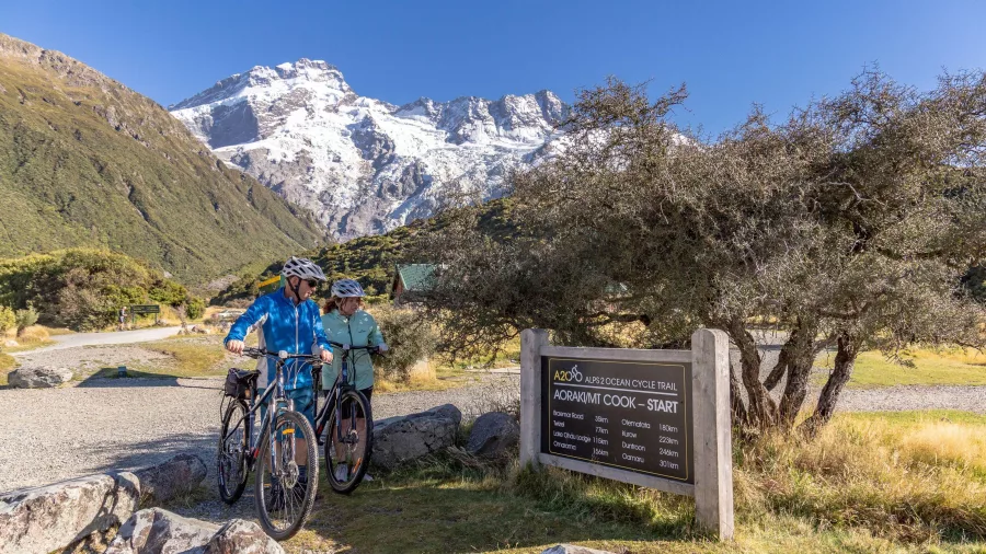 Two cyclists setting off from the official start sign of the Alps 2 Ocean Trail near Aoraki/Mt Cook.