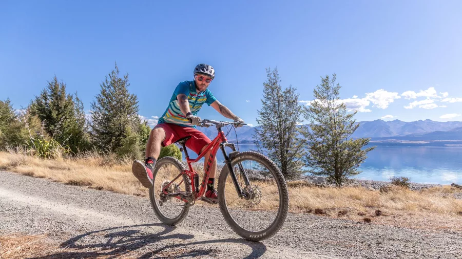 Cyclist performing a wheelie on a gravel trail above Lake Pukaki.