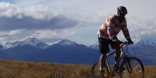 Mountain biker rides through golden tussock in high country terrain near Omarama.
