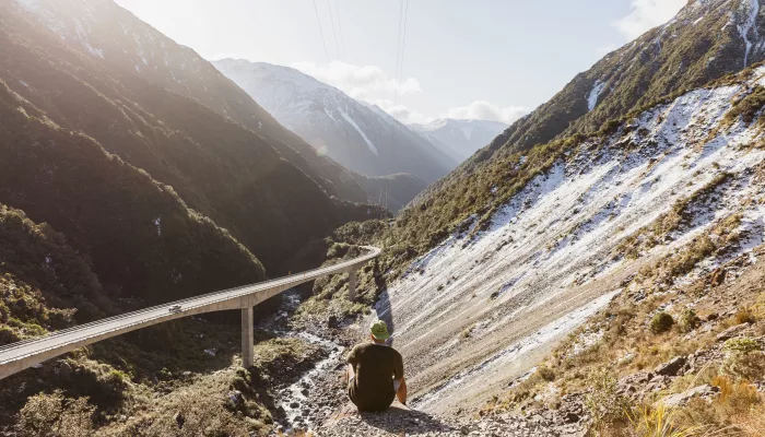 Traveller sitting above the Otira Viaduct with mountains and valley views in Arthur’s Pass