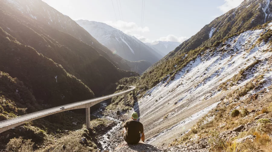 Traveller sitting above the Otira Viaduct with mountains and valley views in Arthur’s Pass