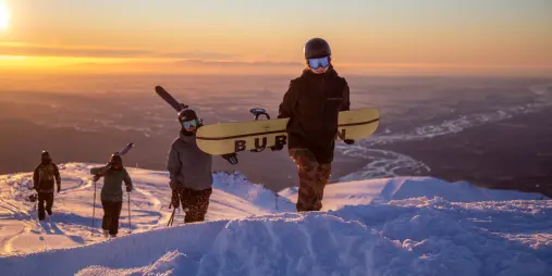 Group of snowboarders and skiers hiking Mt Hutt at sunrise with snow-covered ridgeline and plains below