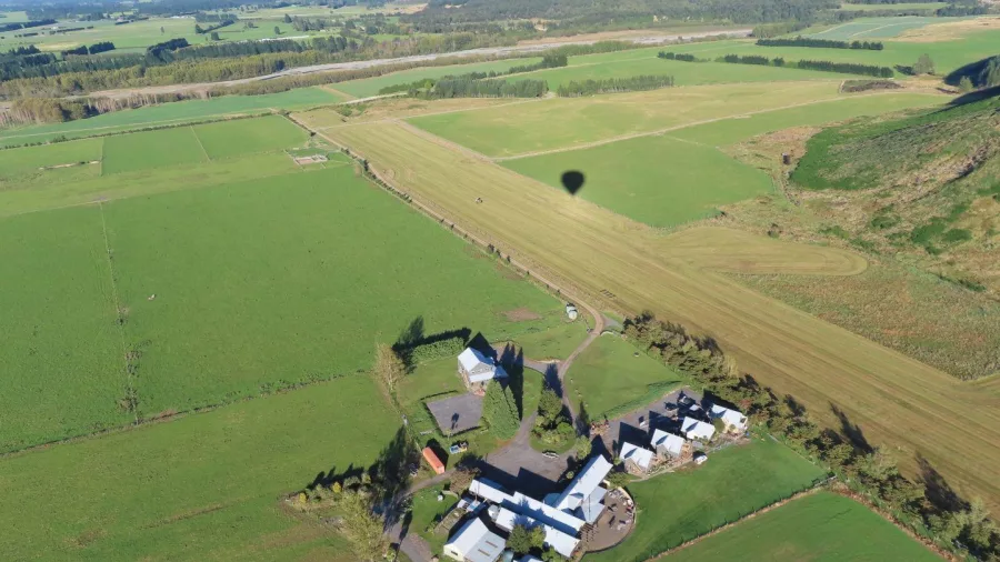 Hot air balloon shadow over Canterbury Plains farmland and buildings