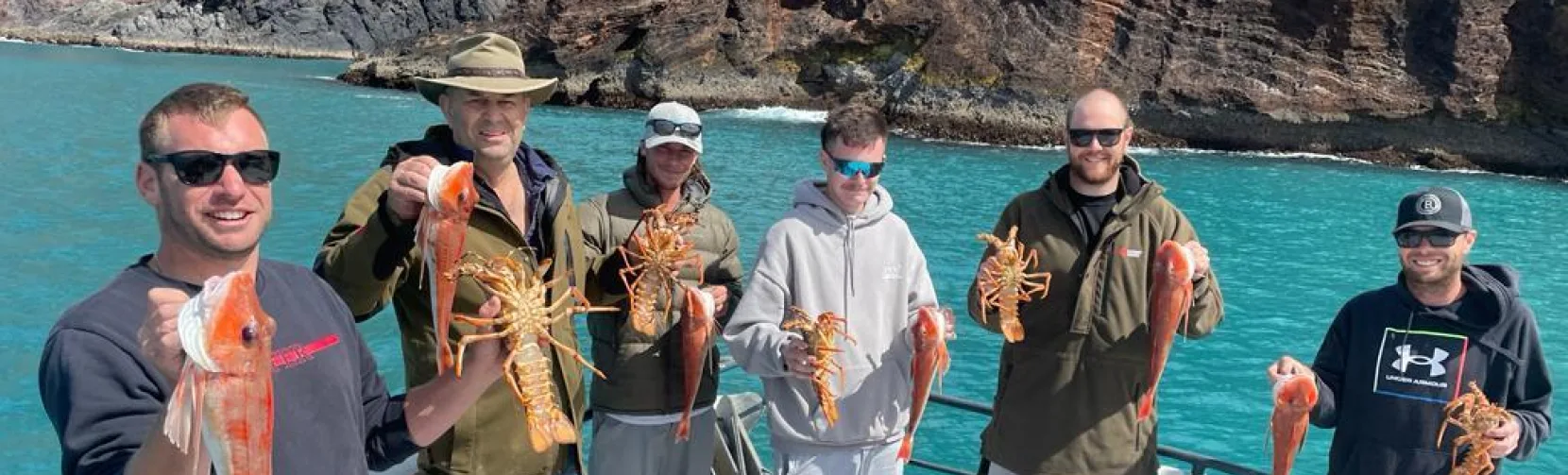 Group holding freshly caught crayfish and red gurnard aboard a fishing charter in Akaroa