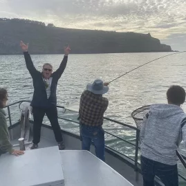 Excited group on a boat as one person reels in a fish in Akaroa Harbour