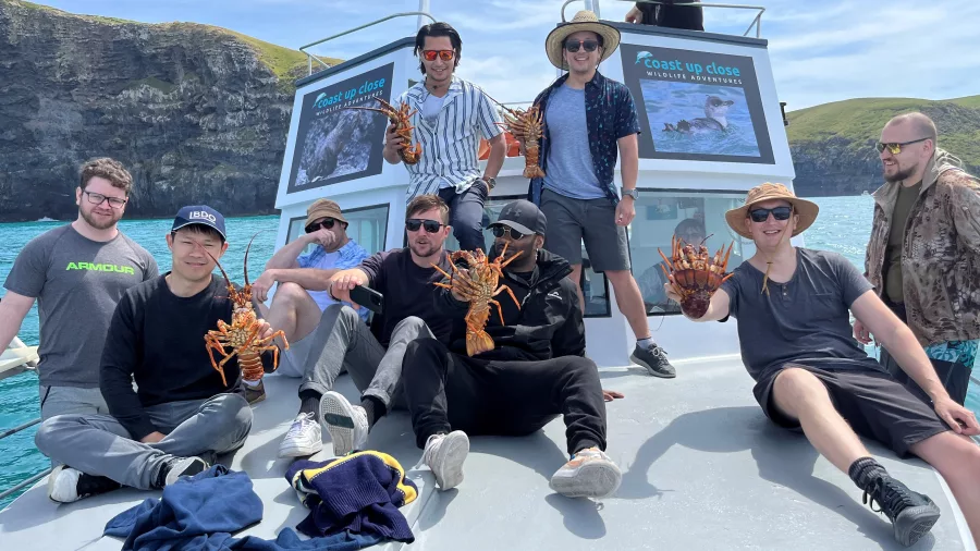 Group of friends showing off their crayfish catch on the deck of a Coast Up Close charter boat