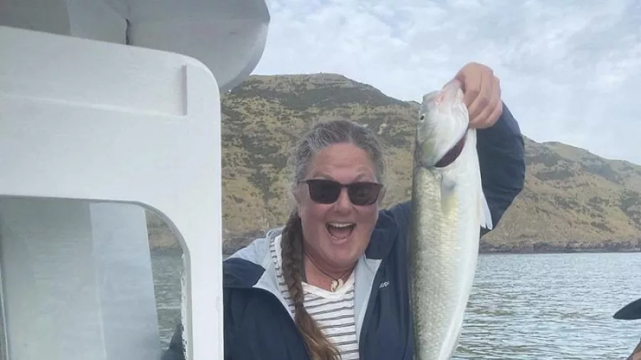 Woman holding a silver fish proudly on a fishing boat in Akaroa Harbour