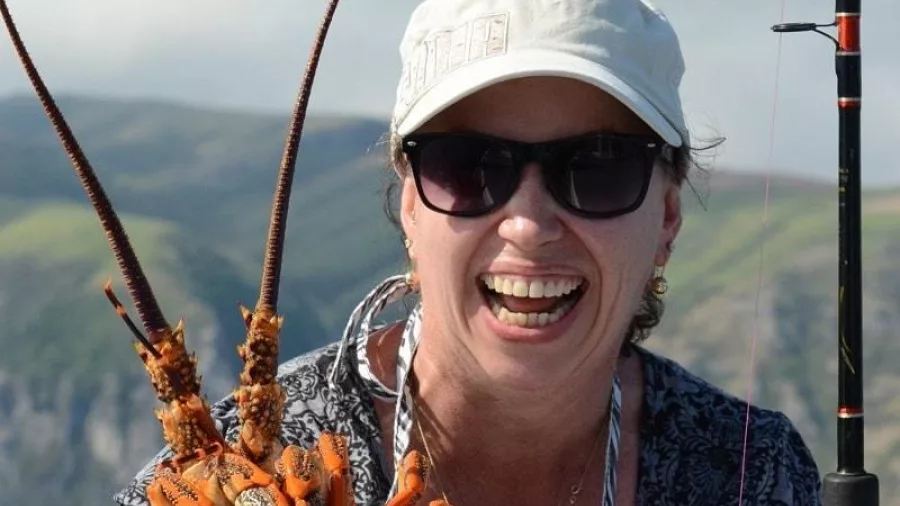 Woman smiling and holding up a freshly caught crayfish on a fishing charter in Akaroa