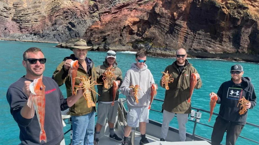Group holding freshly caught crayfish and red gurnard aboard a fishing charter in Akaroa