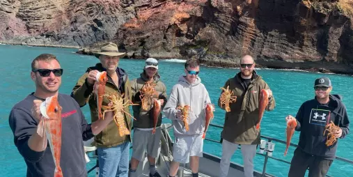 Group holding freshly caught crayfish and red gurnard aboard a fishing charter in Akaroa