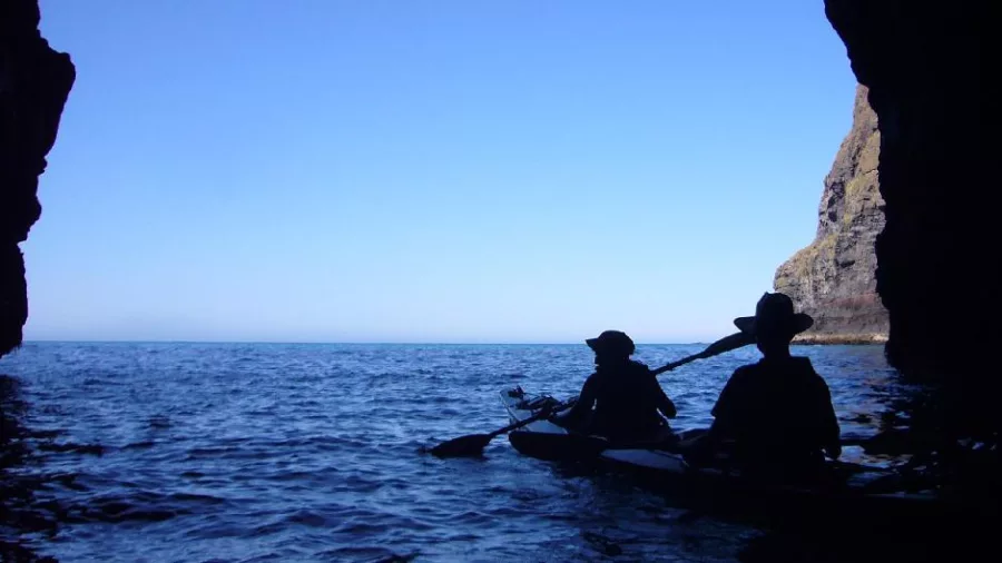 Silhouettes of kayakers emerging from a cave into the open sea in Akaroa