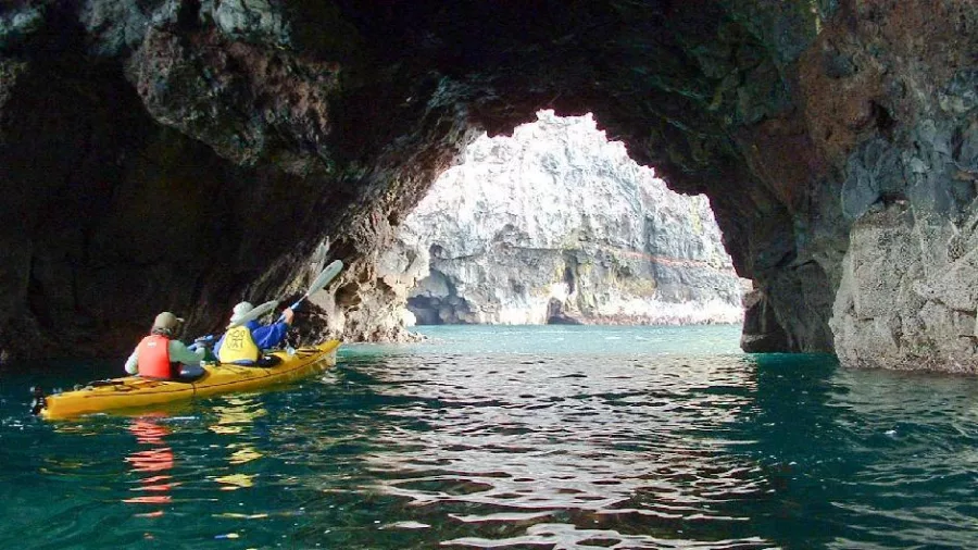 Kayakers entering a large sea cave with light shining through the opening at Pohatu Marine Reserve