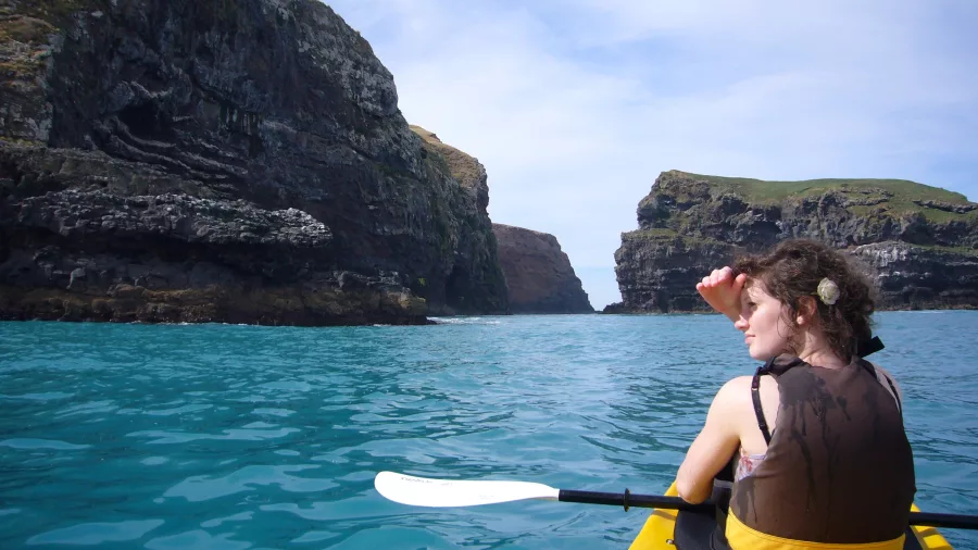 Woman looking ahead from a yellow kayak surrounded by volcanic cliffs in Akaroa