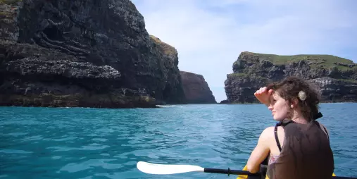 Woman looking ahead from a yellow kayak surrounded by volcanic cliffs in Akaroa