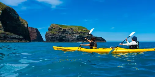 Two kayakers paddling past towering coastal rock formations at Pohatu Marine Reserve