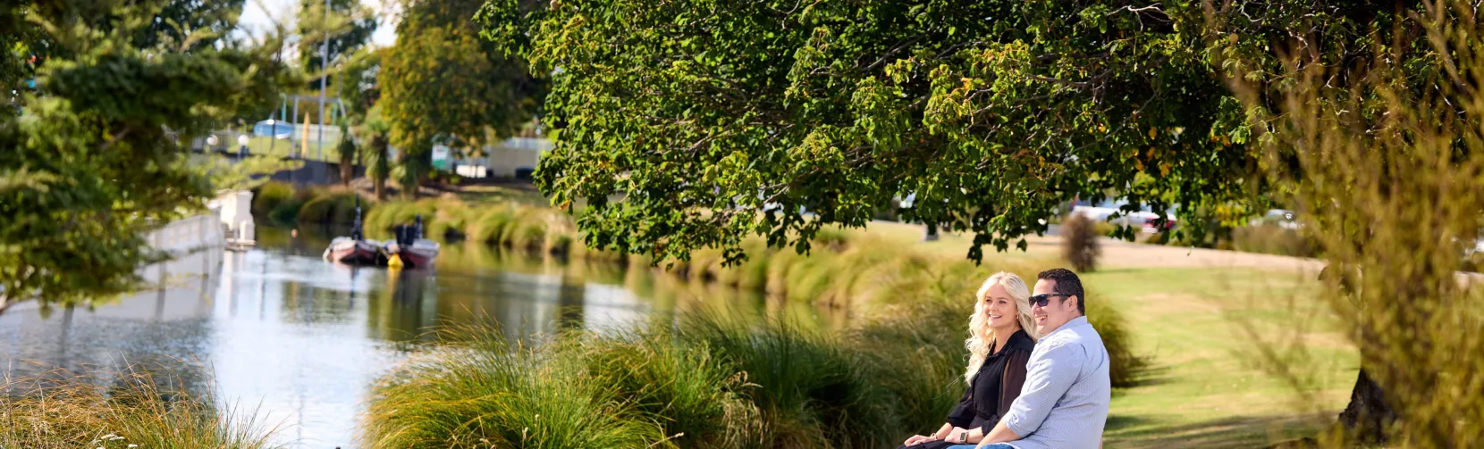 Couple sitting beside the Avon River in Hagley Park, Christchurch