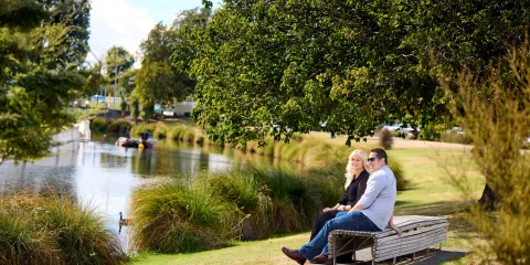 Couple sitting beside the Avon River in Hagley Park, Christchurch