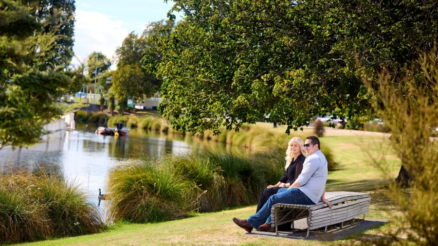 Couple sitting beside the Avon River in Hagley Park, Christchurch