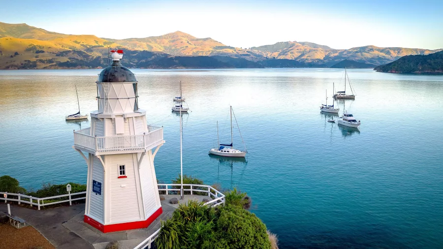 Akaroa lighthouse overlooking calm harbour with anchored sailboats