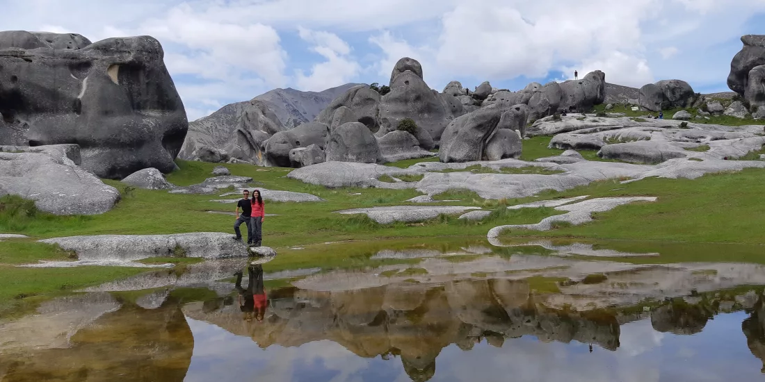 Two people standing beside a still pool reflecting the boulders of Castle Hill