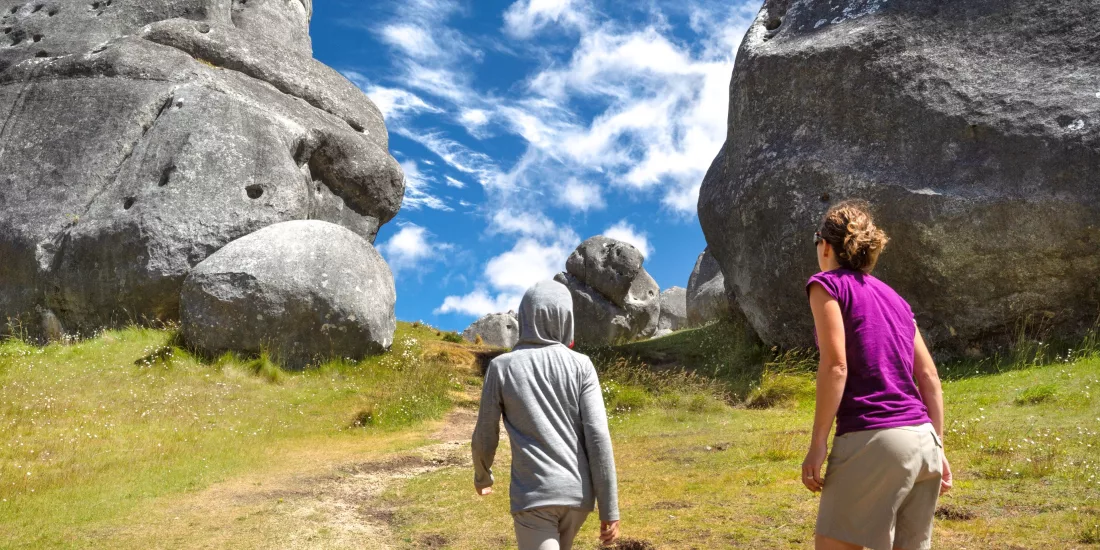 Woman and child walking beneath towering limestone boulders at Castle Hill on a clear day