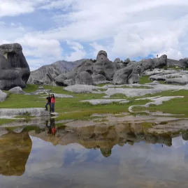Two people standing beside a still pool reflecting the boulders of Castle Hill