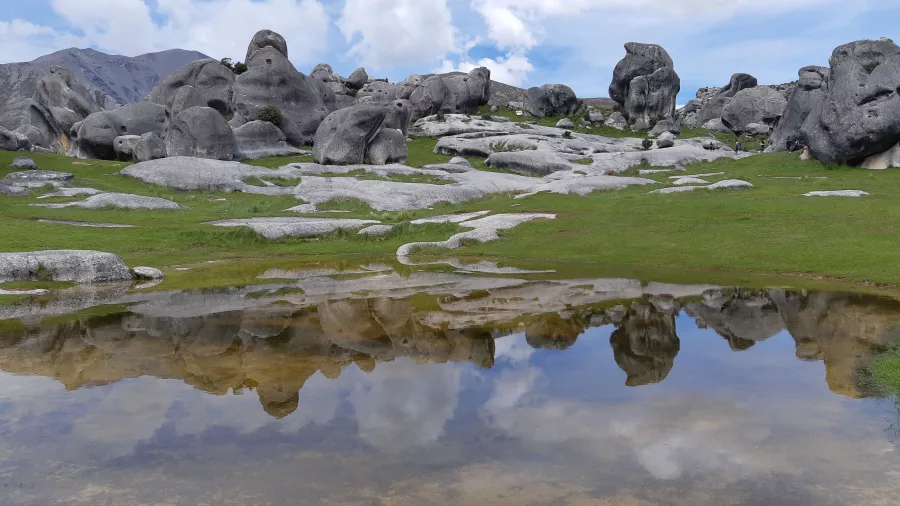 Limestone boulders at Castle Hill reflecting in a shallow pool under a bright sky in Canterbury, New Zealand