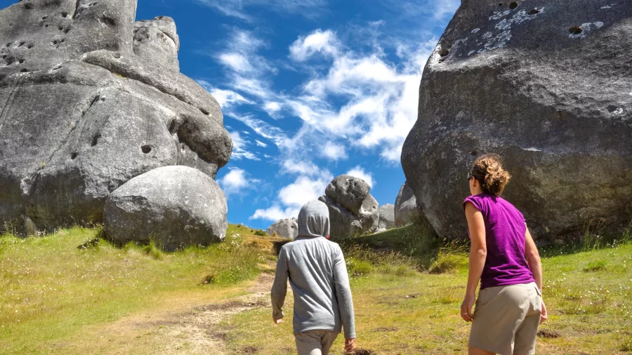 Woman and child walking beneath towering limestone boulders at Castle Hill on a clear day