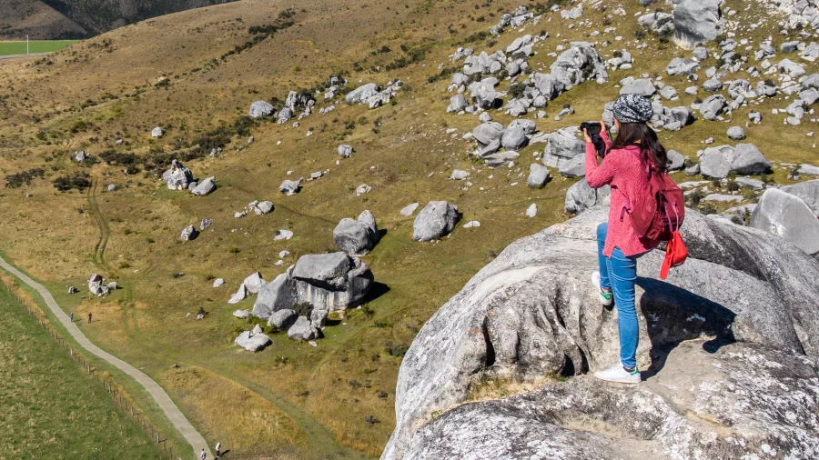 Woman taking photos from atop a limestone boulder overlooking Castle Hill and surrounding plains