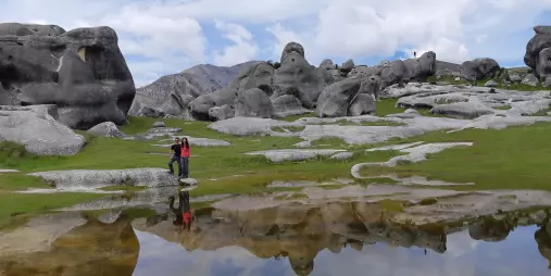 Two people standing beside a still pool reflecting the boulders of Castle Hill