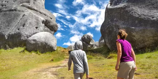 Woman and child walking beneath towering limestone boulders at Castle Hill on a clear day