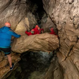 Adventurers navigating rock formations and water in a narrow cave system