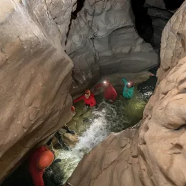 Group of people walking through flowing water in a narrow limestone cave in Canterbury