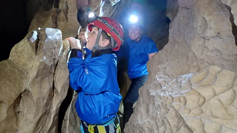 Child and mother wearing helmets exploring narrow cave walls in Cave Stream