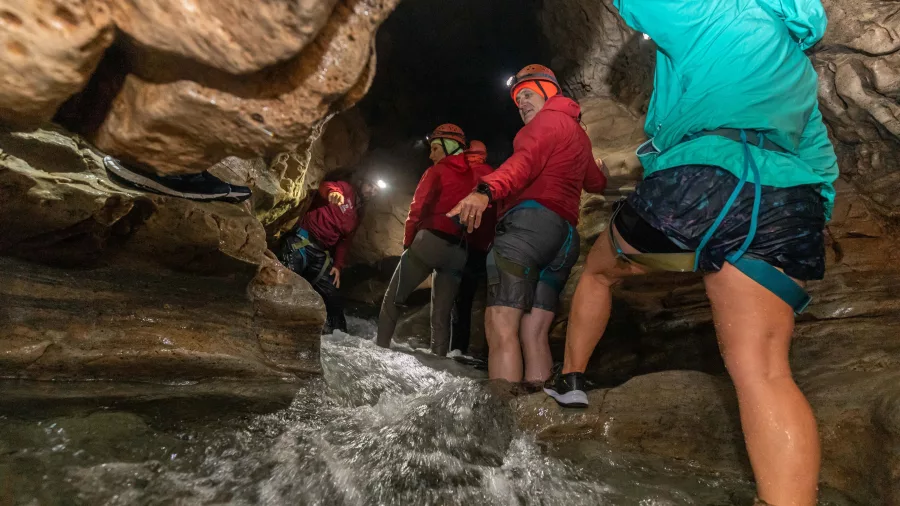 Group wearing helmets and headlamps hiking through shallow water in Cave Stream