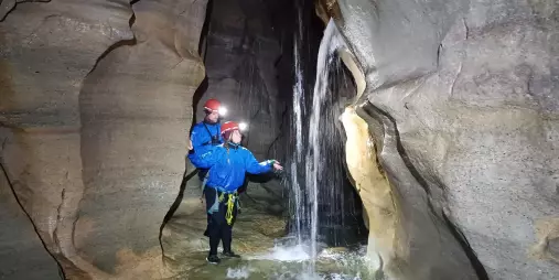 Two cavers in helmets exploring a small waterfall inside Cave Stream, Canterbury