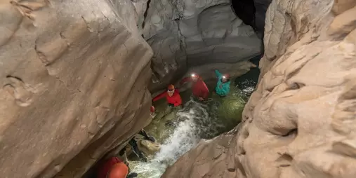 Group of people walking through flowing water in a narrow limestone cave in Canterbury