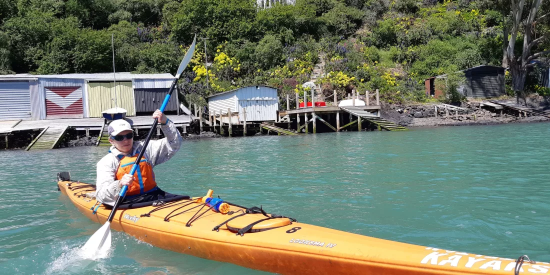 Kayaker paddling past waterfront baches near Diamond Harbour