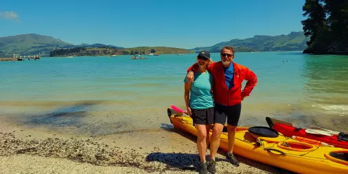 Couple standing by tandem kayak on Quail Island beach with turquoise water behind