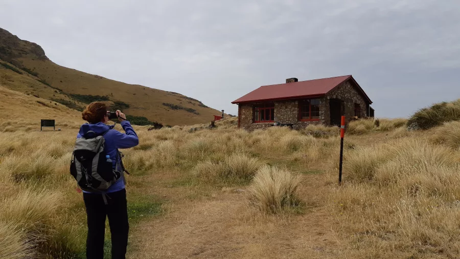 Female hiker photographing the Packhorse Hut from the main trail