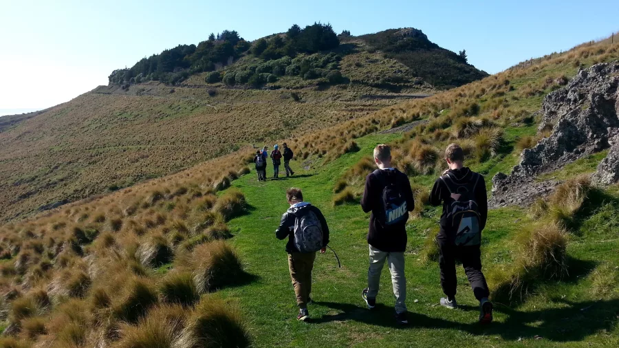 Small group of hikers ascending grassy ridge on Port Hills near Christchurch